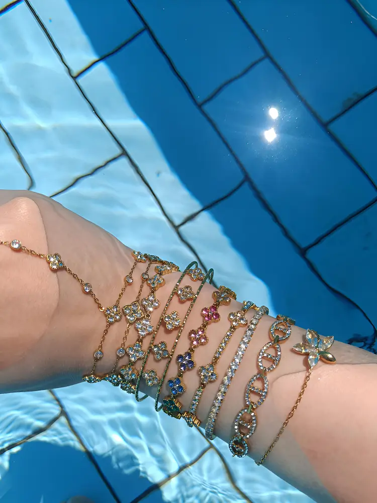 Poignet portant plusieurs bracelets dorés Kyra dans l’eau d’une piscine